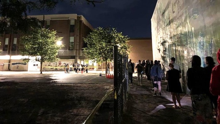 Many voters are lining up by a fence outside polling station in Montreal as night falls.