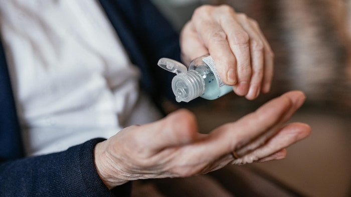 Une femme âgée se verse du liquide désinfectant sur la main.