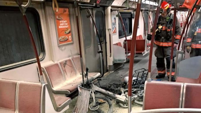 Dans un wagon de métro, un pompier regarde les dommages causés par un vélo électrique ayant pris feu. 