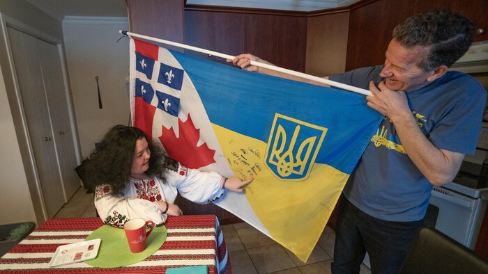 Un homme tient un drapeau mi-ukrainien, mi-canadien au côté d'une femme souriante.