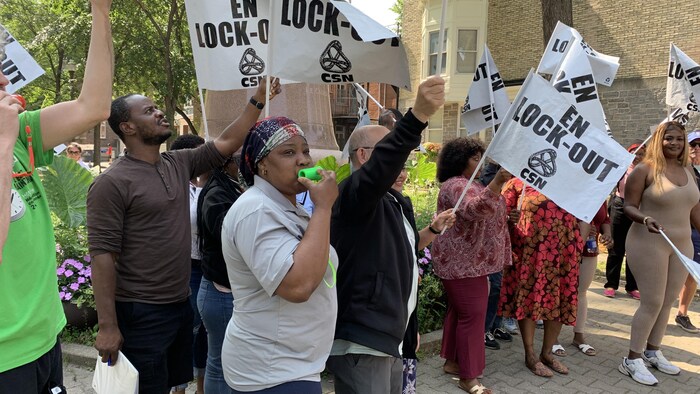 Des personnes manifestent et agitent des affiches sur lesquelles sont &eacute;crits les mots &laquo; En lock-out &raquo;.