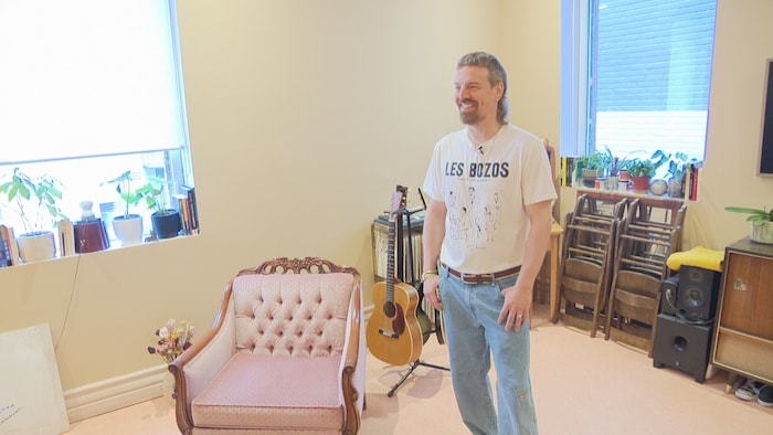 Un homme se tient dans une loge d'artistes devant une chaise, des instruments et des haut-parleurs. 