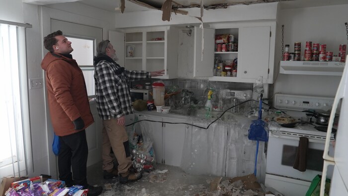 Deux hommes sont dans une cuisine lourdement endommagée par de la glace.