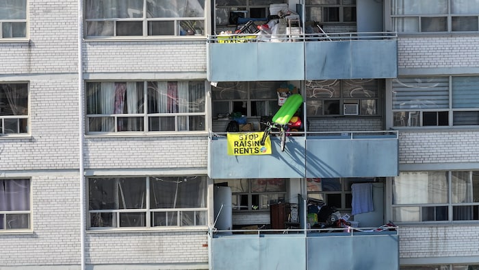 Une vue aérienne de six balcons d'un immeuble à appartement. L'un des balcons à une pancarte avec les mots Arrêtez d'augmenter les loyers.