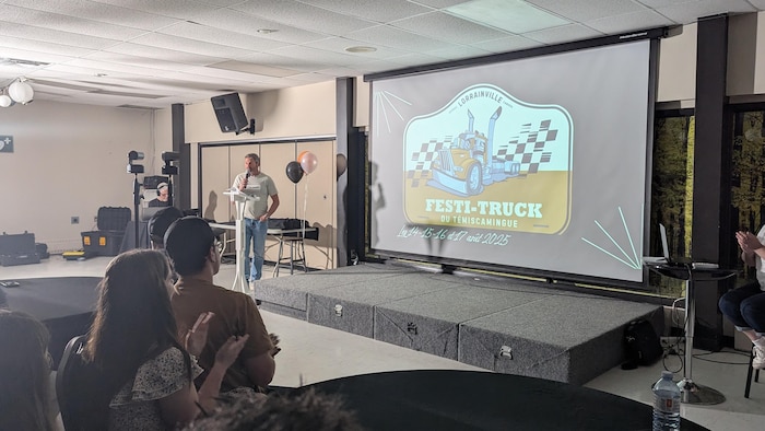 Des gens applaudissent le nouveau logo représentant un camion et des drapeaux de course.