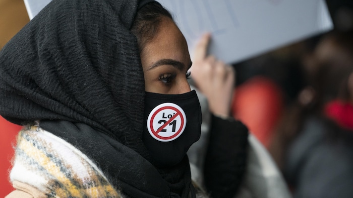Une opposante à la loi 21 portant une tuque, un masque et un macaron.