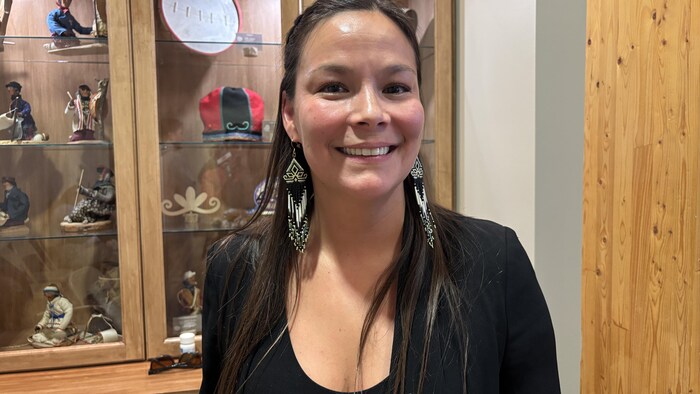 Une jeune femme portant des boucles d'oreilles en billes sourit à la caméra.