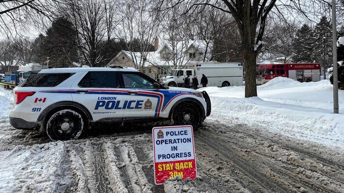 Une voiture de police est stationnée avec un panneau demandant aux automobilistes de rester à distance de sécurité dans une rue enneigée.