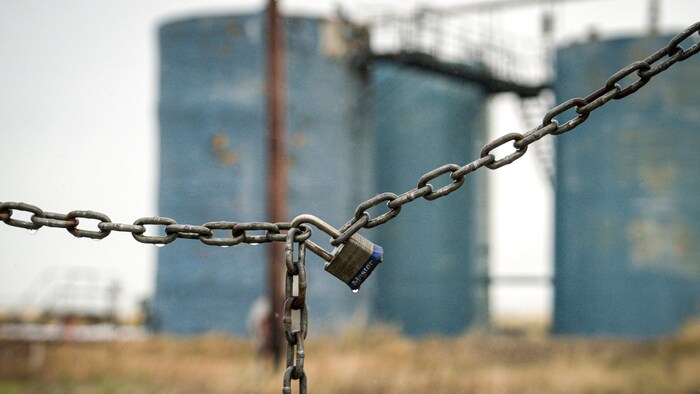 Dans le fond des silos de pétroles abandonnés, une chaîne avec un cadenas au premier plan en bloque l'accès.