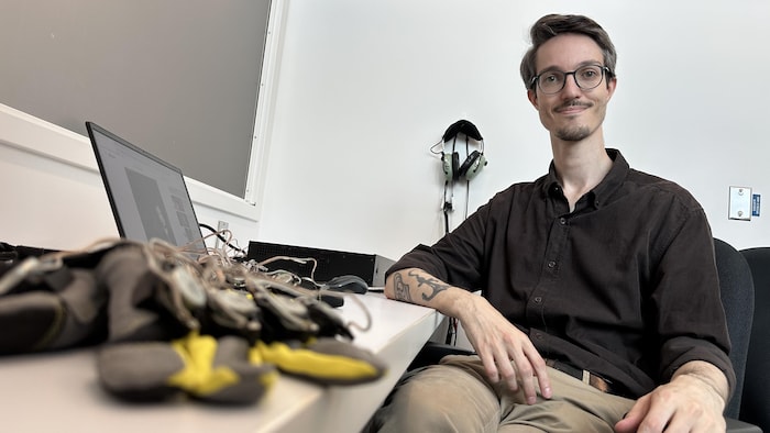 Loonan Chauvette est assis à son bureau. Un gant posé devant son ordinateur.