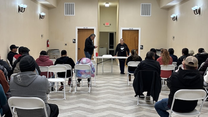 Une femme debout parle à des gens dans une salle. 