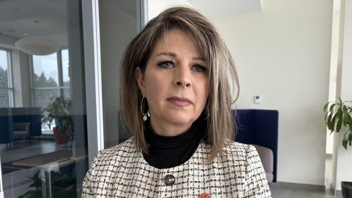 Une femme debout dans un bureau terne, près d'une baie vitrée.