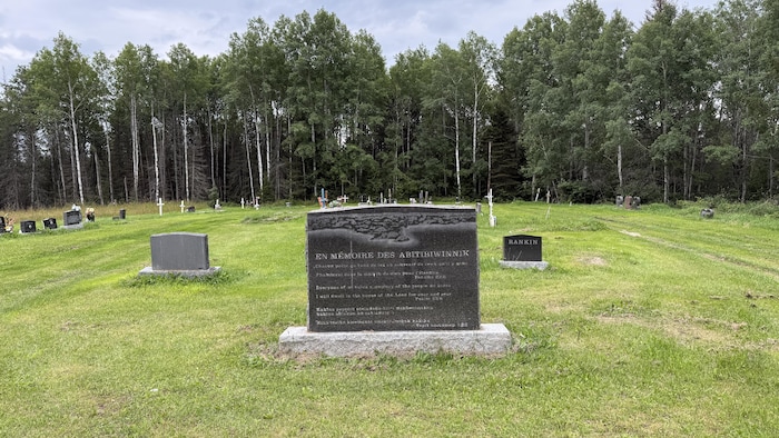 Des pierres tombales dans un cimetière, avec un boisé à l'arrière.