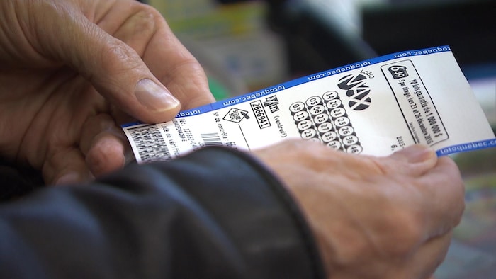 Un homme tient un billet de Lotto Max.