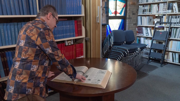 Louis Audet, le président de la Société d’histoire et de généalogie de La Matanie, regarde un recueil d'articles de journaux.