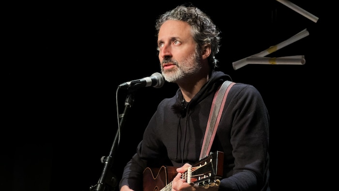 Louis-Jean Cormier, avec sa guitare, chante dans un micro.