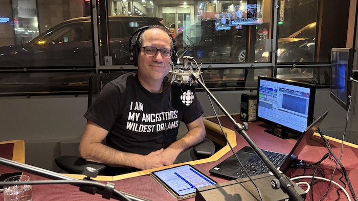 Un homme derri&egrave;re un micro dans un studio radio.