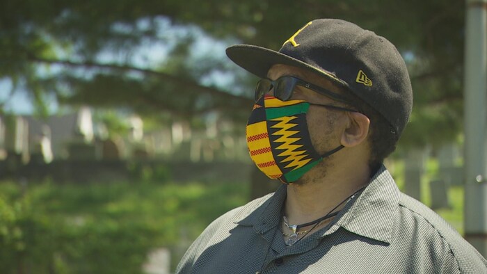 Un homme, avec une casquette, portant un masque, à l'extérieur.