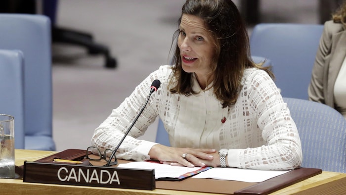 Une femme prend la parole devant un micro et un bureau identifié «Canada».