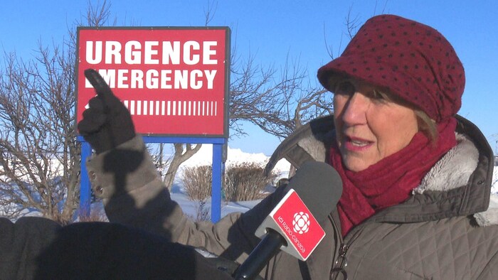 Louise Blanchard en hiver devant l'affiche indiquant l'entrée de l'urgence.
