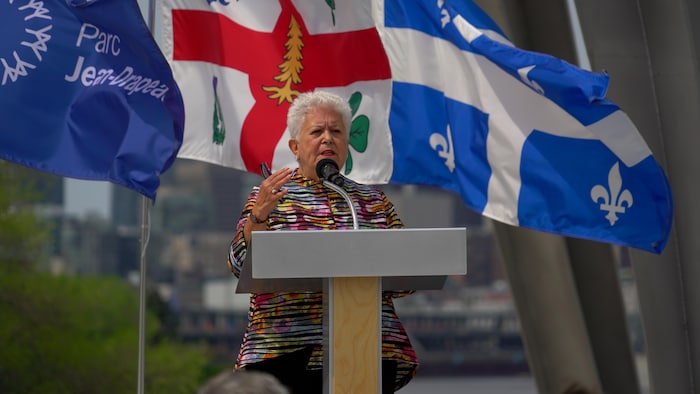 Mme Harel livrant un discours devant les drapeaux du Québec, de Montréal et du parc Jean-Drapeau.