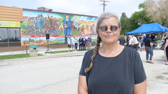 Louise Perret-Gentille pose devant la murale de Louis Riel et de l'abbé Noël Ritchot à Saint-Norbert.