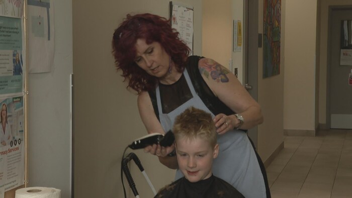 Une femmes coiffe un jeune garçon. 