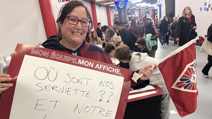 Sophie Pilon avec une affiche sur laquelle est écrit "Où sont nos serviettes et notre logo" et un drapeau de la Victoire.