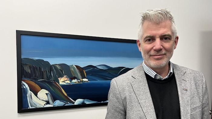 Luc Boivin devant un tableau accroché au mur.