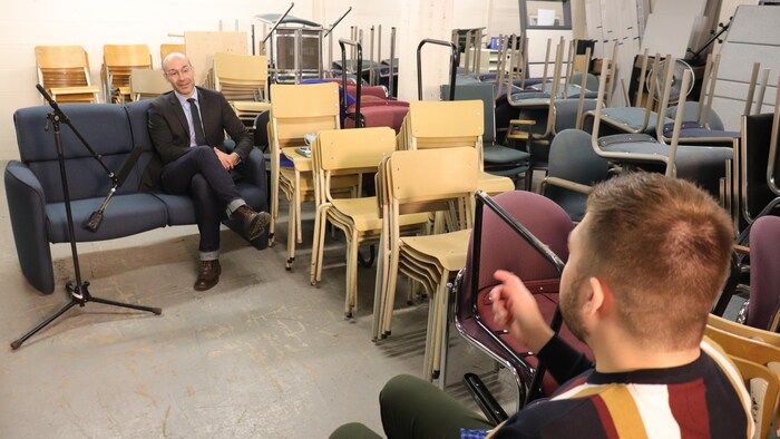 Le professeur en management de l'Université Laval, Luc Bres, au travers de chaises empilées dans un entrepôt.