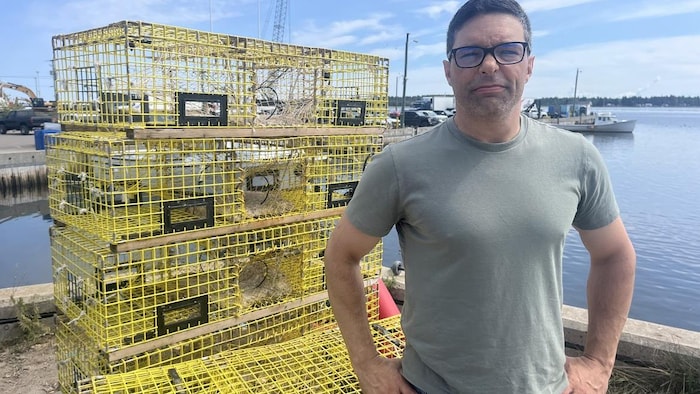 Un homme devant des casiers à homard.