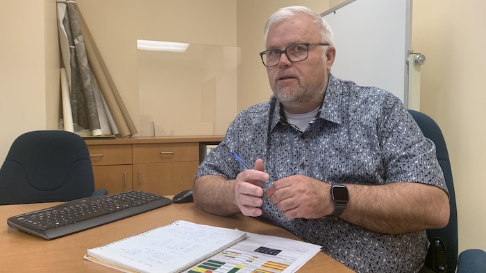Luc Tremblay, assis derrière son bureau, parle, un stylo en main, des documents posés sur son bureau.