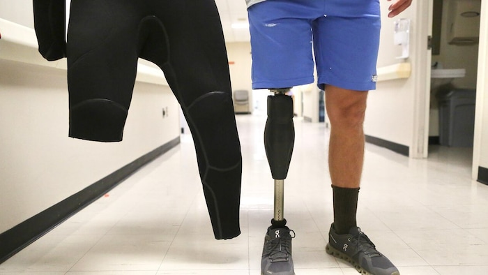 Gros plan de la jambe amputée d’un surfeur et de son vêtement en main adapté à sa blessure. 