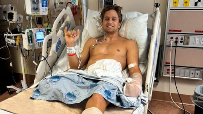 Lucas Arsenault dans un lit d'hôpital fait un signe de la main. 