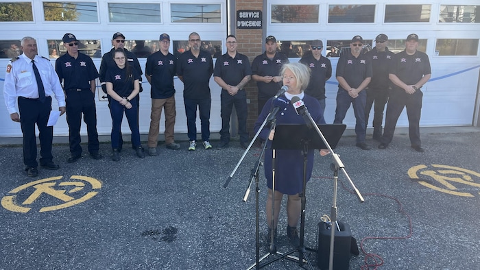 Luce Daneau parle dans un micro. Derrière elle, les pompiers de proximité de sa municipalité.