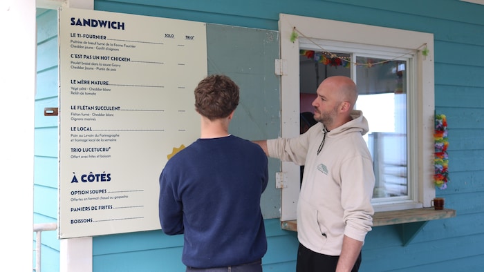 Tommy Roy explique quelque chose à son apprenti, devant le menu de la cantine.