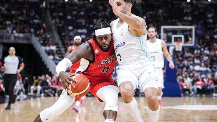Un basketteur tient le ballon, l'épaule baissée, et entrant en contact avec un rival.