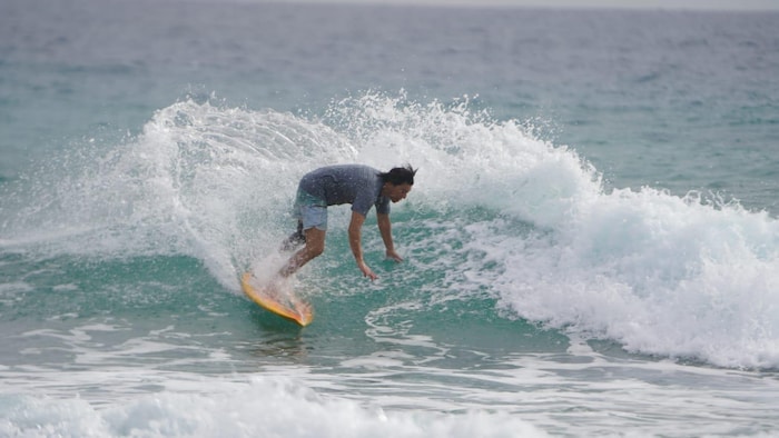 Un surfeur en short et chandail exécute un virage serré sur une planche au cœur d'une vague déferlante.