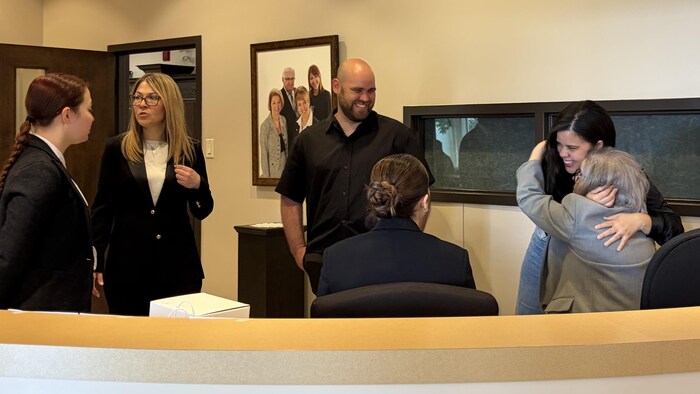Liliana, debout, fait une accolade chaleureuse à une dame assise pendant que Luis sourit.