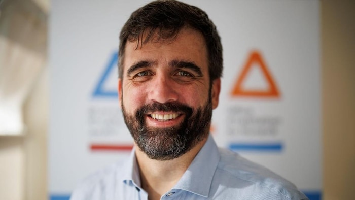 Lupin Daignault souriant est devant un panneau.