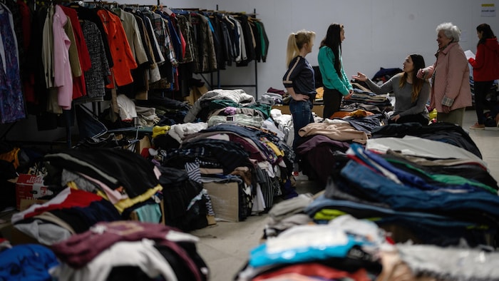 Quatre femmes discutent au milieu d'un entrepôt bondé de vêtements.
