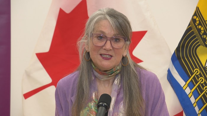 Lyne Chantal Boudreau parle au micro, des drapeaux du Canada et du Nouveau-Brunswick derrière elle.