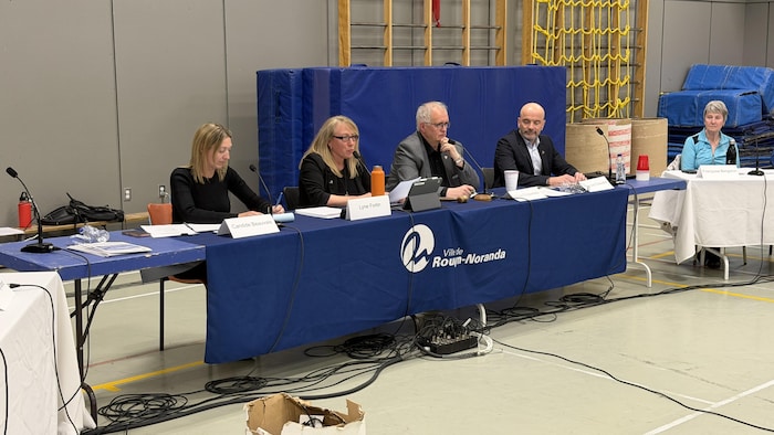 Lyne Fortin, Gilles Chapadeau et François Chevalier assis à une table dans un gymnase.