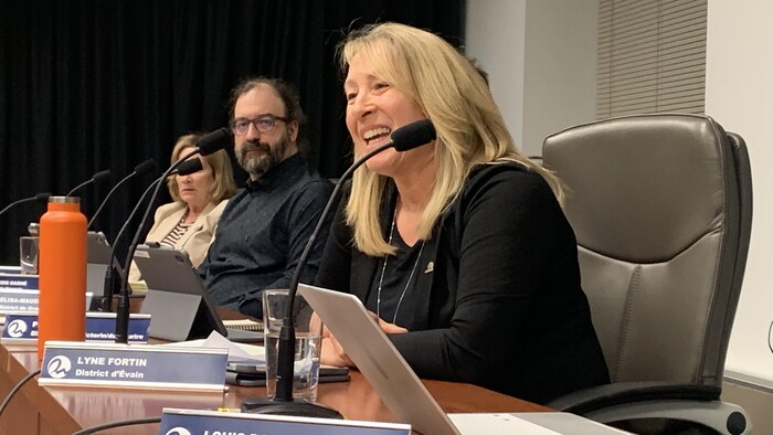 Lyne Fortin, assise à son siège en assemblée du conseil municipal, parle au micro en souriant.