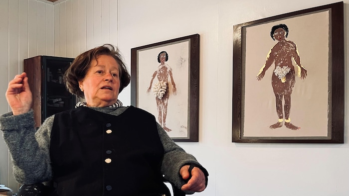 La femme est assise dans son atelier, devant deux de ses toiles.