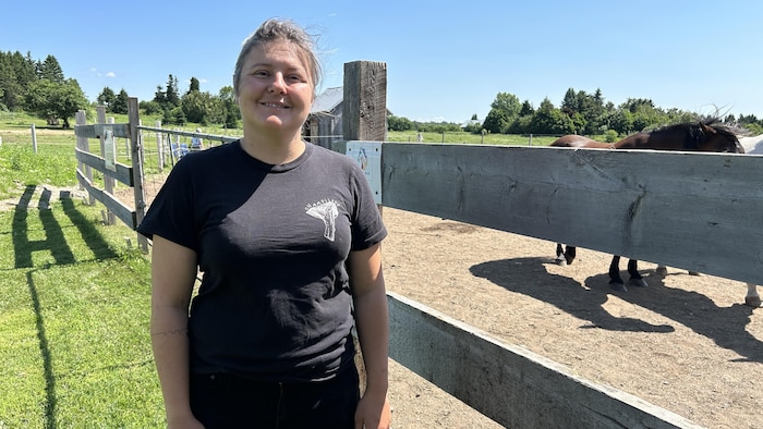 Une femme regarde l'objectif à côté d'un enclos à cheval.