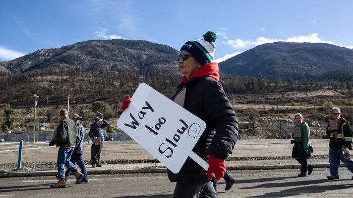 Une manifestante âgée tient une pancarte sur laquelle est écrit : « Vraiment trop lent ». 