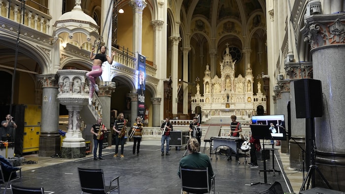 Une acrobate suspendue en l'air s'entraîne au-dessus de musiciens qui jouent dans la nef d'une église.