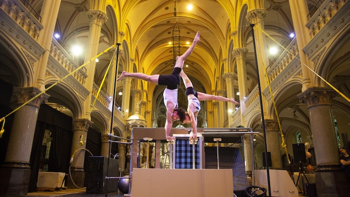 Deux acrobates exécutent une figure d'équilibre simultanée sur des cannes fixées à une structure relevée.