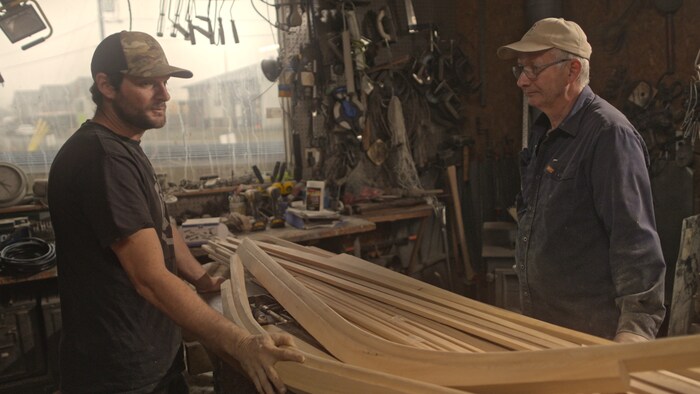 Deux hommes autour d'un canot en bois en construction.
